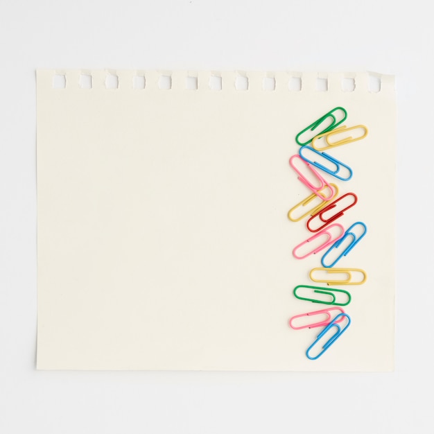 Яркие разноцветные скрепки на бумаге на белом фоне