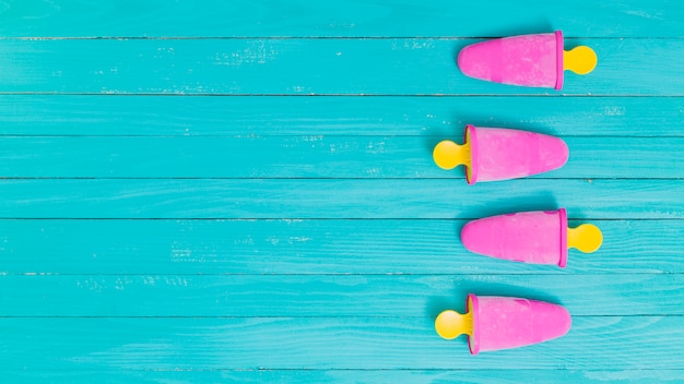 Free photo bright pink frozen popsicles on yellow sticks on wooden background