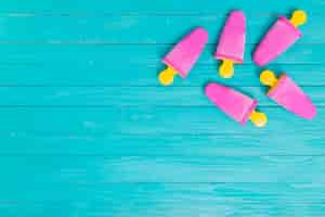 Free photo bright pink popsicles on yellow sticks on wooden background