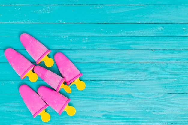 Bright pink popsicles on yellow sticks on wooden turquoise background