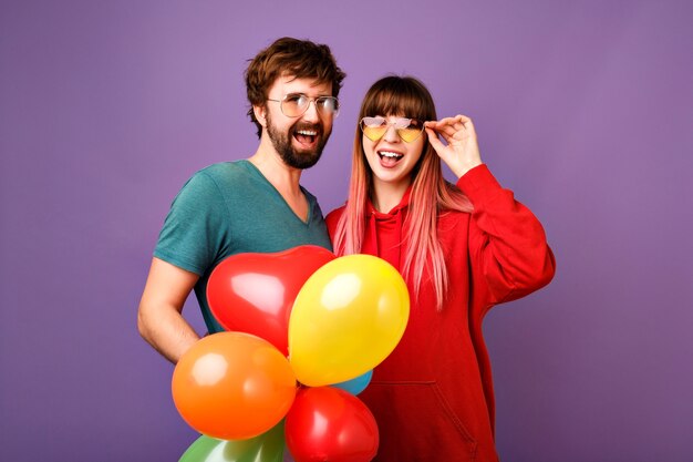 Bright positive  lifestyle portrait of couple hipsters having fun, showing tongues and holding party air balloons, best friends together, casual sportive clothes