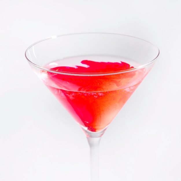 Ярко-красный цвет растворяется в прозрачном бокале для мартини на белом фоне