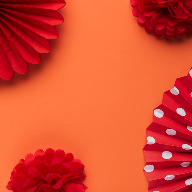 Ярко-красный декоративный поддельный цветок и бумажный веер на оранжевом фоне