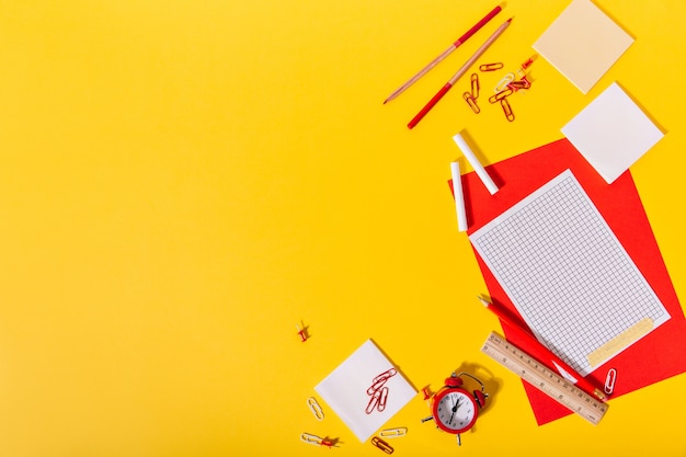 Яркий набор школьных принадлежностей, состоящий из красного и бумаги, скрепок, мелков, карандашей и деревянной линейки.