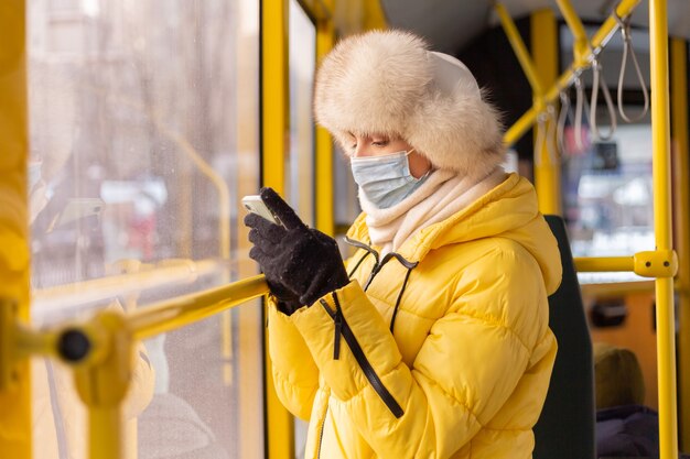 Ritratto luminoso e soleggiato di una giovane donna in vestiti caldi in un autobus urbano in una giornata invernale con un telefono cellulare in mano