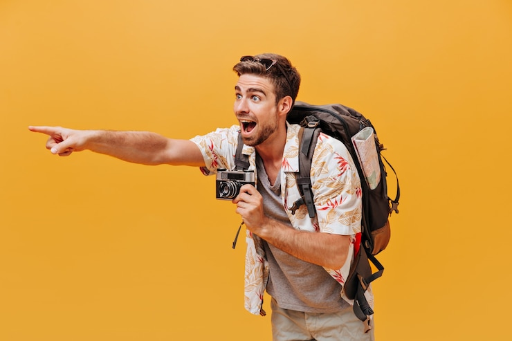 Free Photo bright tourist with ginger beard in white cool shirt and grey t-shirt showing aside his finger and holding camera on isolated wall