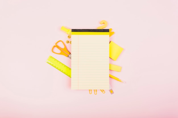 Free photo bright yellow office supplies behind empty notepad