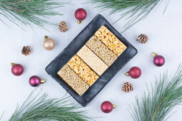 Brittle candies on black plate with Christmas ornaments. 