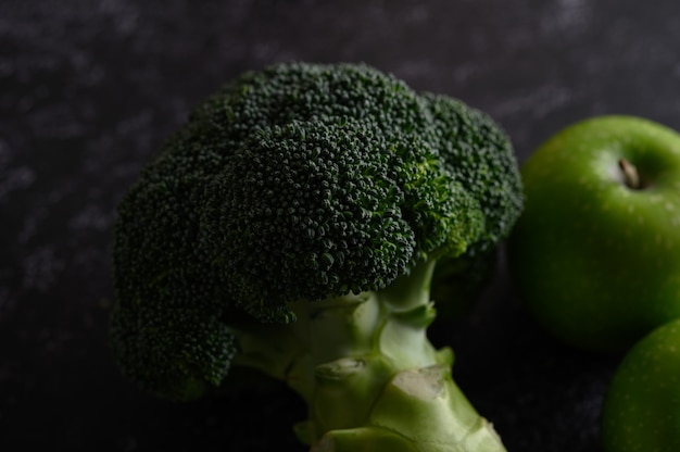 Broccoli, Apple, and avocado on a black cement floor.