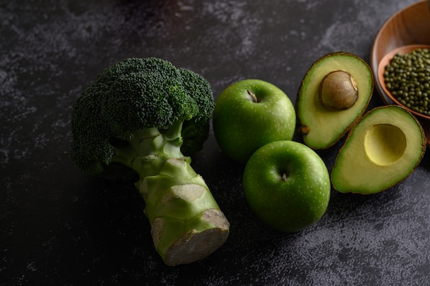 Broccoli, Apple, and avocado on a black cement floor.