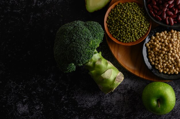 Broccoli, Apple, and legumes on a black cement floor.