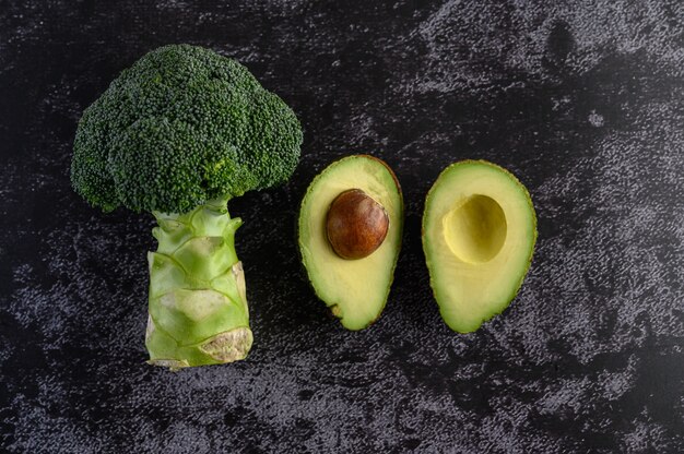 Broccoli and avocado on a black cement floor.