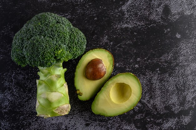 Broccoli and avocado on a black cement floor.