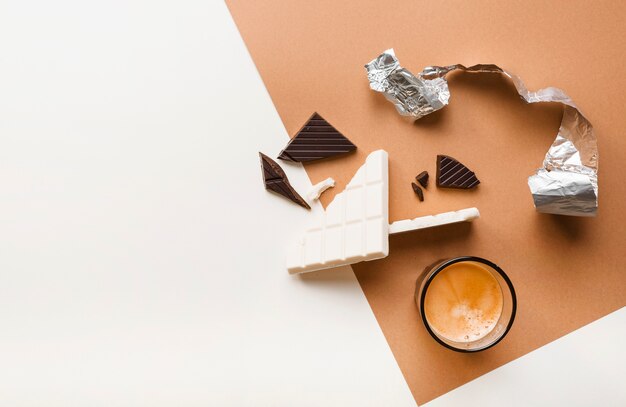 Rotti tavolette di cioccolato scure e bianche con un bicchiere di caffè sullo sfondo