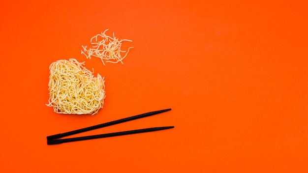 Broken dry instant noodles with chopsticks over orange background
