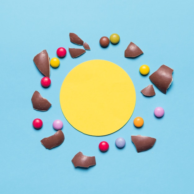 Бесплатное фото Разбитая скорлупа пасхальных яиц и драгоценные камни, окруженные пустой желтой круговой рамкой на синем фоне