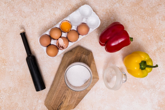 Free photo broken eggshells; oil bottle; sugar jar and bell peppers on textured backdrop