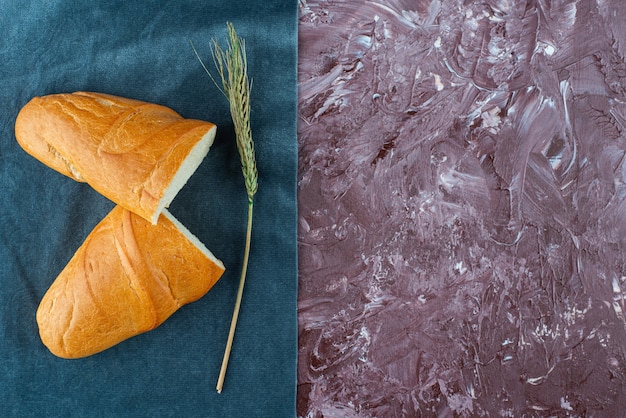 Broken loaf of white bread with wheat ear on a light background. 