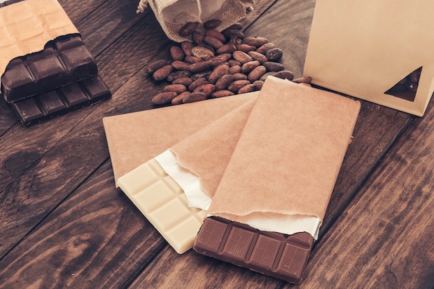 Broken package of dark and milk chocolate bar with cocoa beans on table