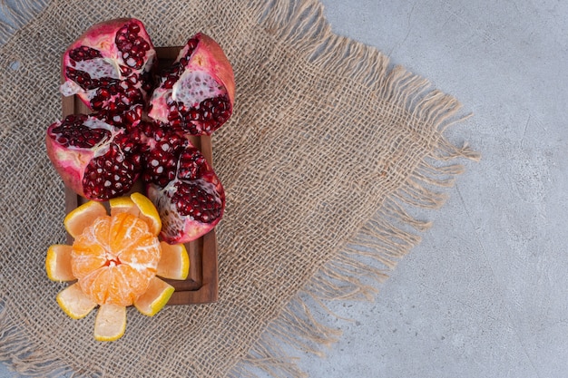 A broken pomegranate and a peeled tangerine on a piece of cloth on marble background. 