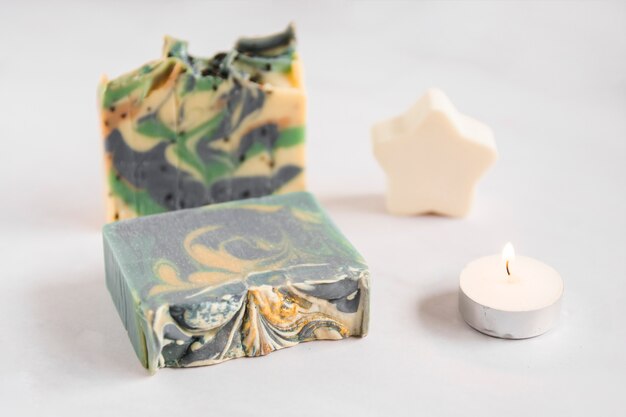 Broken soap bar with star sponge and illuminated candle on white background