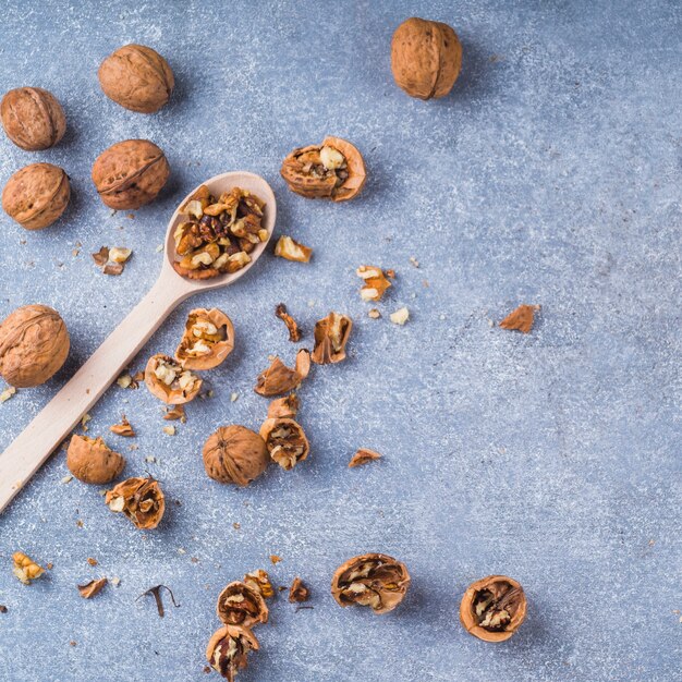 Broken walnuts and kernel on wooden spoon over the textured backdrop