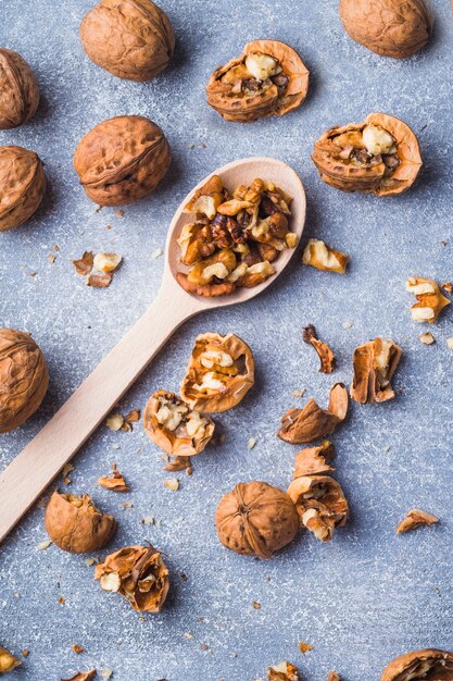 Broken walnuts and kernel on wooden spoon over the textured backdrop