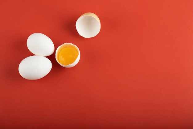 Broken and whole raw eggs on red surface. 