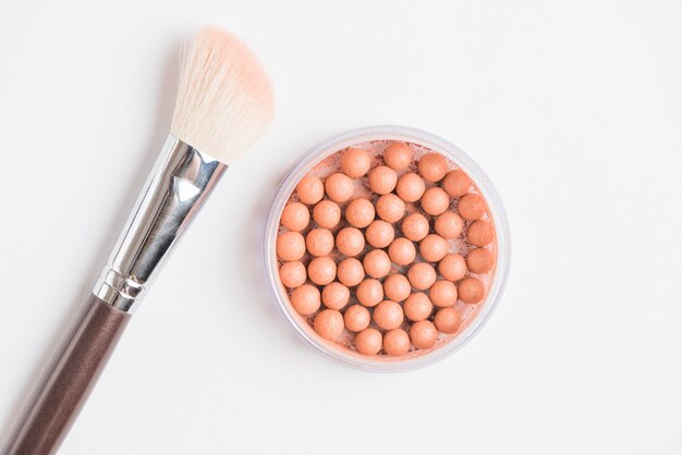 Bronzing pearls with makeup brush on white background