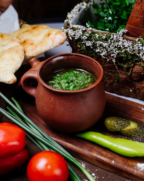 Broth soup with herbs and vegetables in a pottery jar.