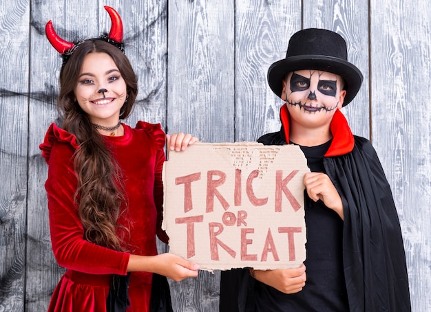 Foto gratuita i fratelli che tengono dolcetto o scherzetto firmano dentro i costumi di halloween