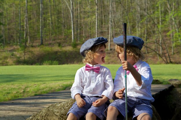 Brothers with funny faces in a golfing field surrounded by greenery under the sunlight