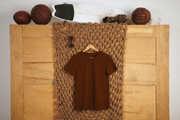 Brown basic cotton t-shirt presented in rustic interior with vintage leather play balls on top