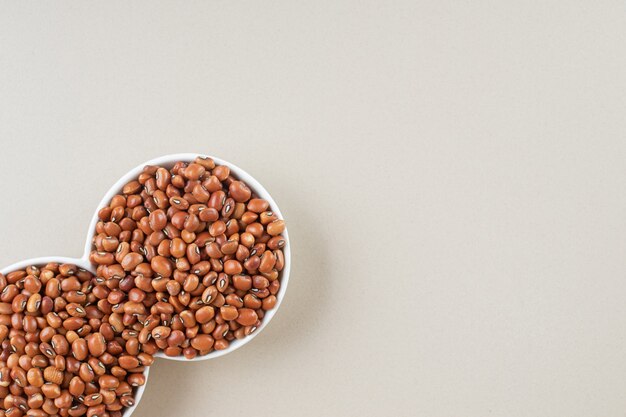 Brown beans in a ceramic cup on concrete.