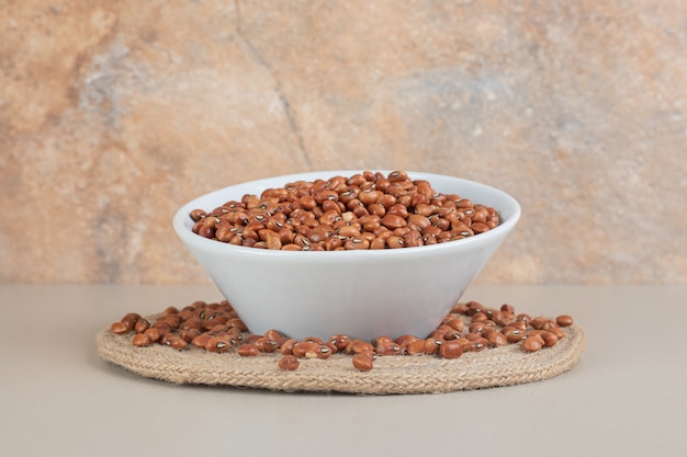 Brown beans in a ceramic cup on concrete.