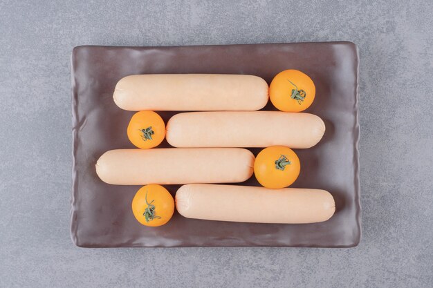 A brown board of boiled sausages with cherry yellow tomatoes 