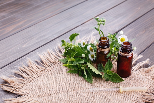 Brown bottles with oils, greenery and flowers lie on brown napkin