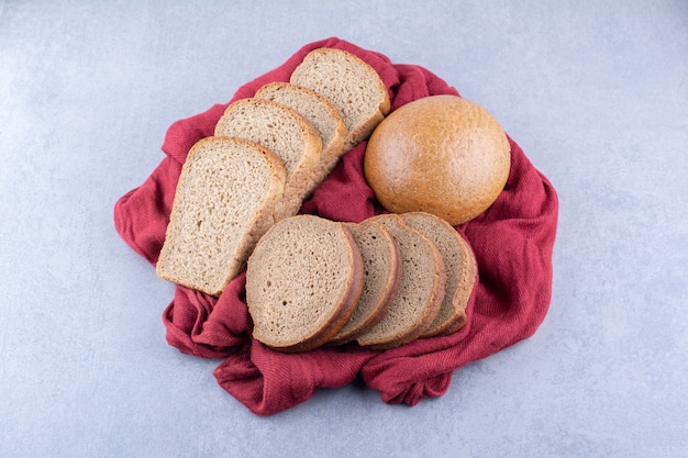 Brown bread slices and a bun on a cloth piece on marble surface