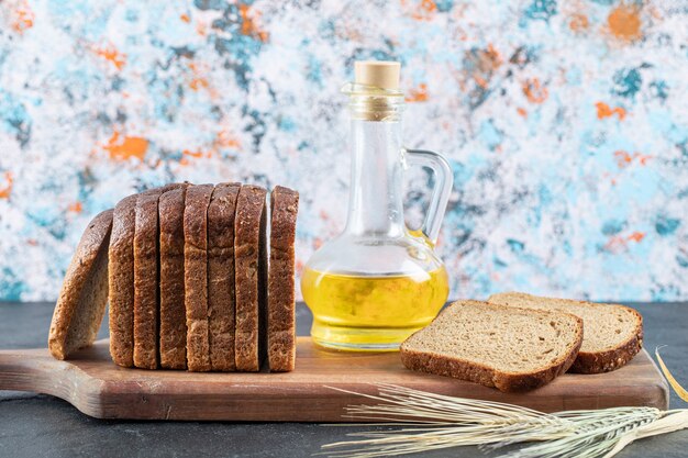 Ломтики коричневого хлеба и бутылка масла на деревянной доске.