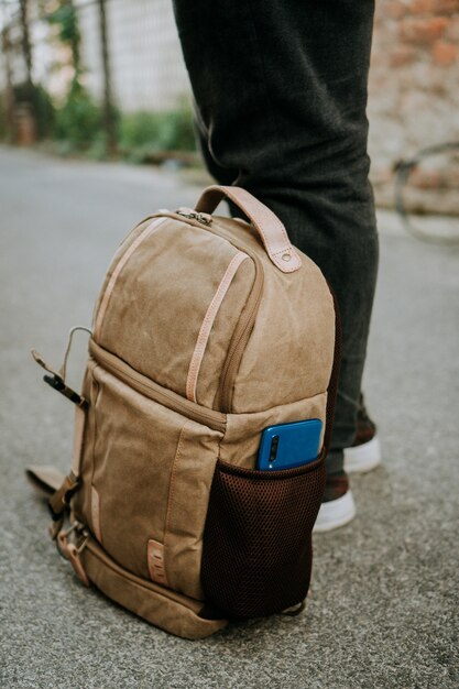 Brown canvas camera bag with a smart phone in the side pocket, on the ground