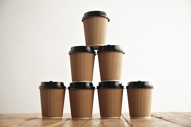 Brown cardboard take away paper cups with black caps in pyramid house shape on rustic vintage table in center of picture