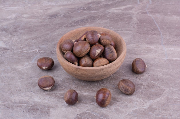 Castagne marroni in una tazza di legno su marmo.