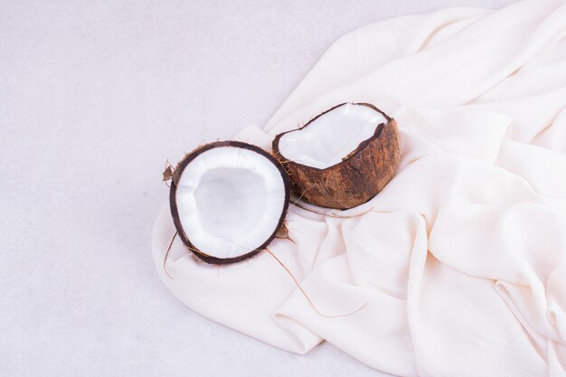 A brown coconut cut into two pieces on a white towel