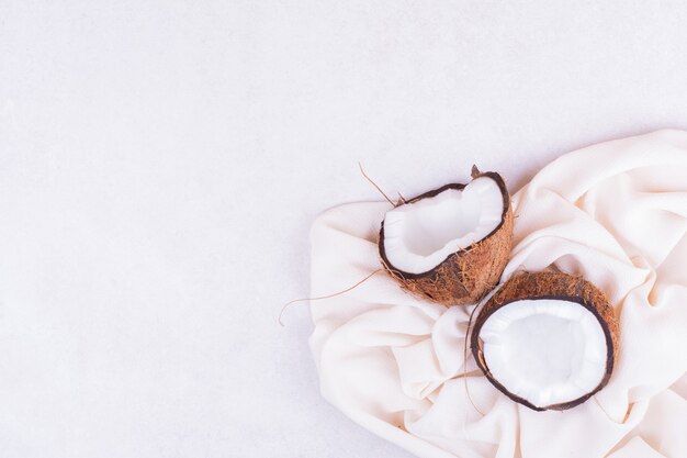 A brown coconut cut into two pieces on a white towel