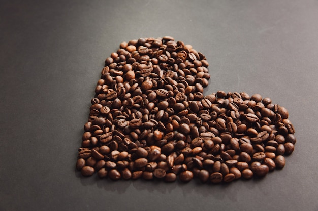 Brown coffee beans in form of heart isolated on black texture background for design. saint valentine's day card on fabruary 14, holiday concept.