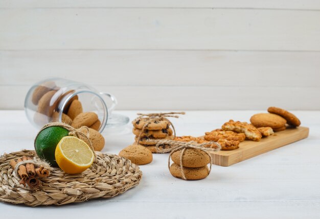 Brown cookies  in glass jar with cookies on a cutting board and citrus fruits on a round placemat on white surface