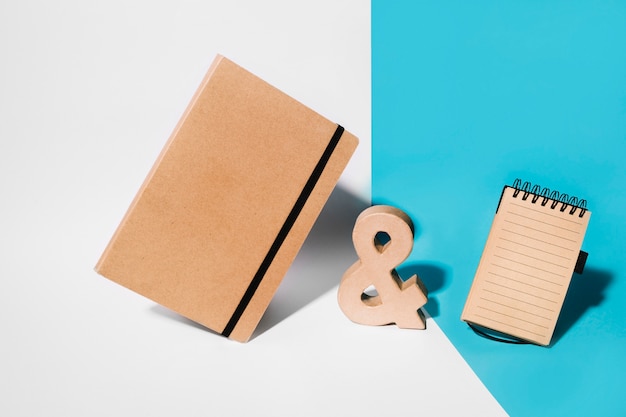 Brown cover notebook; wooden ampersand sign and spiral notepad on white and blue background