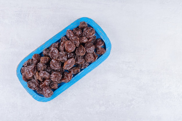 Brown dried cherries inside a dish on concrete surface