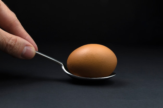 黒​の​背景​に​分離された​手​で​保持された​スプーン​に​茶色​の​卵