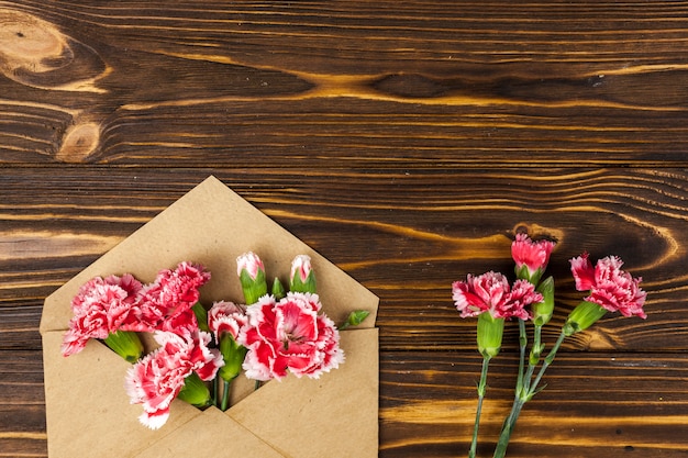 Brown envelope and red carnation flowers on wooden table